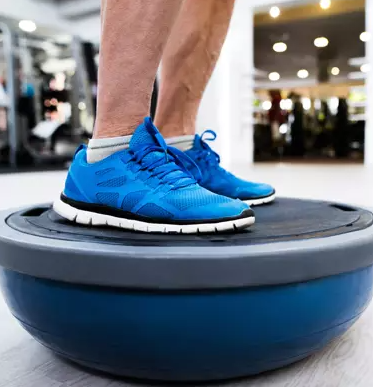 Patient in blue sneakers balancing on a medicine ball at the gym
