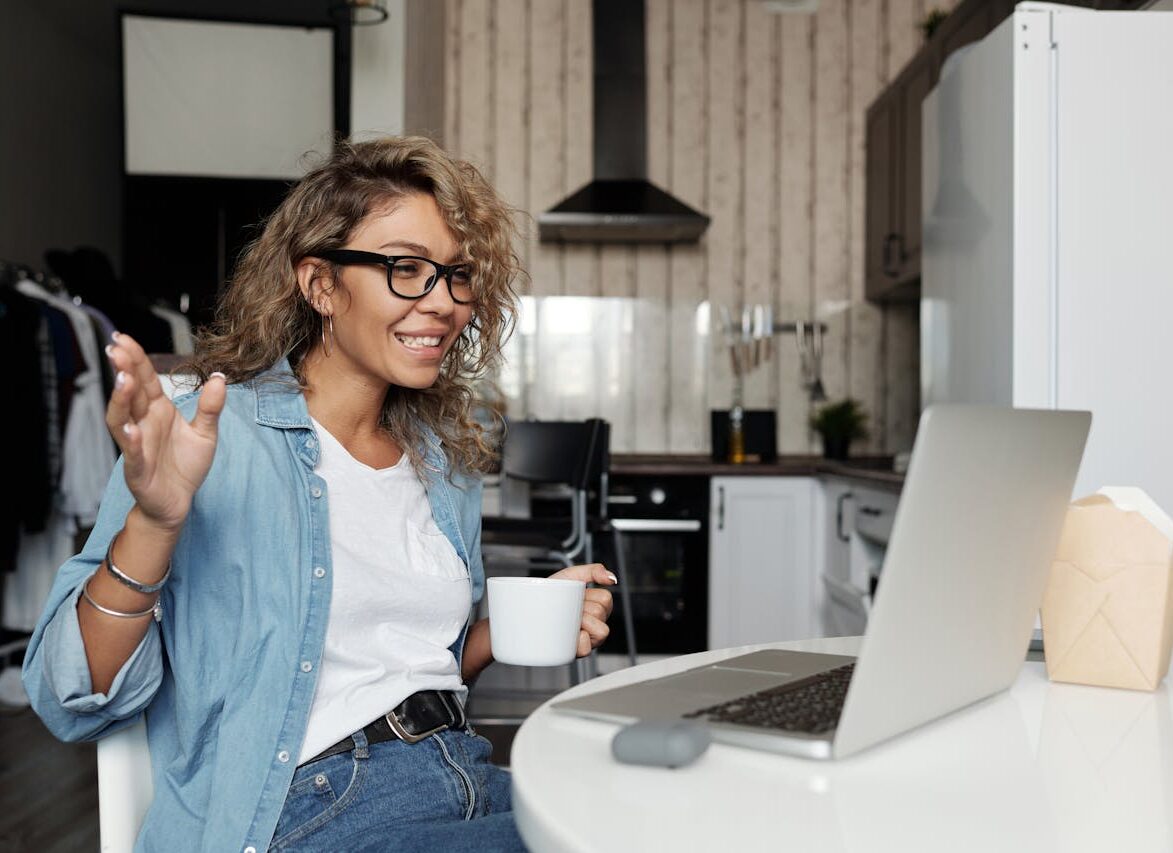 Woman in her kitchen drinks coffee and speaks with a friend through the computer