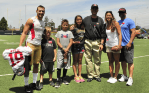 Former NFL player and Legacy Donor Devon Wylie smiles on a football field with his family and Jim Harbaugh